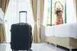 Luggage in modern hotel room with happy young adult female relaxing nearly window, asian woman tourist looking to beautiful nature view. Time to travel, relaxation, journey, trip and vacation concepts