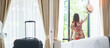 happy young adult female relaxing nearly window, asian woman tourist looking to beautiful nature view with Luggage in modern hotel room. Time to travel, relaxation, journey, trip and vacation concepts