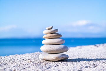 Canvas Print - Closeup shot of pebbles stacked on each other in a balance with the blue sea in the background