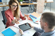 Portrait of two people involved in talk. Man and woman discuss working situation. Modern tablet with black screen. Business papers on desk. Smart qualified workers in office. Job concept
