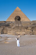 Girl in white dress walking towards the great Sphinx and the Great Pyramid of Giza.