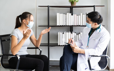 Woman wearing face mask sitting on the armchair and talking to the professional psychologist while wearing face mask conducting a consultation and making notes during coronavirus or COVID 19 outbreak