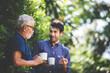 © chokniti - An adult hipster son and senior father talking at home, morning nature scene in the home garden outdoor