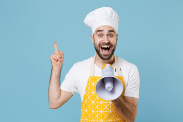 Sticker - Excited young male chef or cook baker man in apron white t-shirt toque chefs hat isolated on blue background. Cooking food concept. Mock up copy space. Screaming in megaphone pointing index finger up.