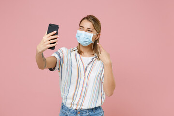 Young girl in casual striped shirt isolated on pink background. Epidemic pandemic coronavirus 2019-ncov sars covid-19 flu virus concept Doing selfie shot on mobile phone pointing on sterile face mask.