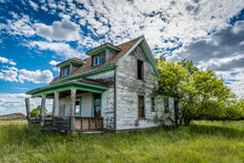 Old, Abandoned Prairie Farmhouse With Trees, Grass And Blue Sky In Saskatchewan, Canada