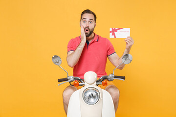 Wall Mural - Shocked young bearded man guy in summer clothes driving moped isolated on yellow background. Driving motorbike transportation concept. Mock up copy space. Hold gift certificate, put hand on cheek.