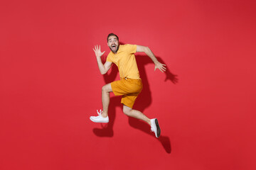 Canvas Print - Side view of excited young bearded man guy in casual yellow t-shirt posing isolated on red background studio portrait. People lifestyle concept. Mock up copy space. Jump like running, spreading hands.