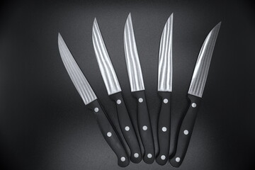 Set of five silver steak knives with black handles on black background