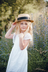 little girl with a straw hat. beautiful little girl with blond hair in a white dress in the background of a beautiful field. Girl with a bouquet of red poppies