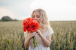 © Олег Кошевський - beautiful little girl with blond hair in a white dress in the background of a beautiful field. Girl with a bouquet of red poppies