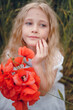 © Олег Кошевський - beautiful little girl with blond hair in a white dress in the background of a beautiful field. Girl with a bouquet of red poppies