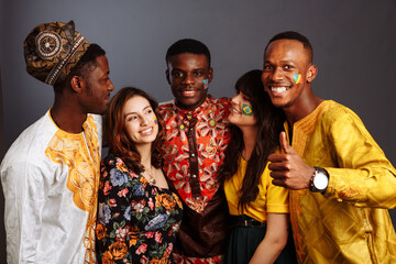 Concept of friendship and peace between countries: three African men and two Latin ladies in national clothes show thumb up hug together with body arts flags Congo, Nigeria, Brazil, Ecuador