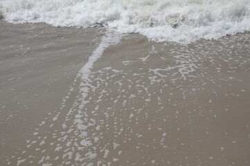 Trail sea wave with white foam on the sandy shore