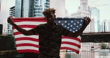 African Ethnicity Man Stay With American Flag And Want Independence  Life Without Racism. Young Protested African American Male Bear The Bridge And Skyscrapers Street In America. 