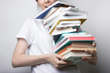 A girl in a white T-shirt holds a lot of books in her hands on a neutral background. Education, training manuals