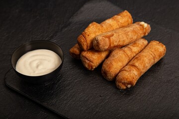 Sticker - Pile of some fried rolls and a bowl of white sauce on the black background