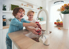 Happy Kids Washing Cherries Under Tap Water At The Kitchen