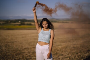 Poster - Horizontal shot of a female posing with a smoke bomb on a background of fields and windmills