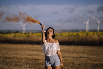 Sticker - Horizontal shot of a female posing with a smoke bomb on a background of fields and windmills