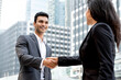 © Atstock Productions - Smiling handsome young Indian businessman making handshake with businesswoman in the city with office buildings in background