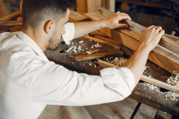 Wall Mural - Man working with a wood. Carpenter in a white shirt. Worker measures a board