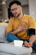 © JustLife - Young man measuring blood pressure. Sick young man in living room.