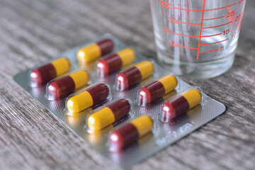 ed-yellow capsule of antibiotics in medicine panel with measuring cup beside on wooden table background