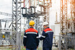 Two specialist electrical substation engineers inspect modern high-voltage equipment during sunset. Energy. Industry