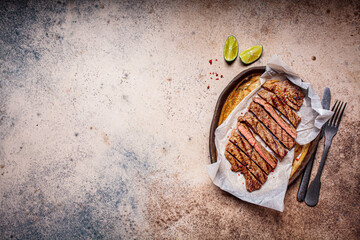 Wall Mural - Sliced grilled beef steak with spices in dark dish, dark background, copy space.