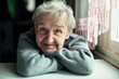 © De Visu - An old elderly woman, smiling portrait, looking at the camera, sitting in the kitchen.