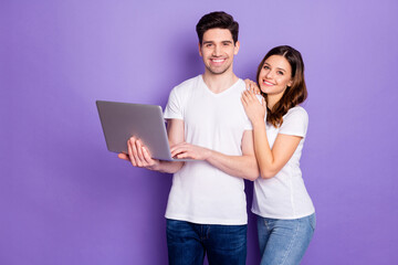 Poster - Portrait of positive couple man woman hold laptop work from home have online partnership communication wear white t-shirt casual style denim jeans isolated over violet color background