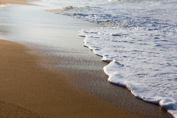 beautiful filled frame close up seascape wallpaper background shot of golden orange sand with white foamy waves of the Indian ocean forming pretty textures and patterns. Pitiwella beach, Sri Lanka