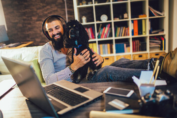 Handsome tattooed man working at home on laptop while sitting at the table with cute dog