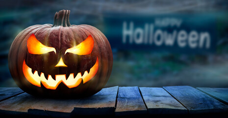 One spooky halloween pumpkin, Jack O Lantern, with an evil face and eyes on a wooden bench, table with a misty night background with space for product placement.