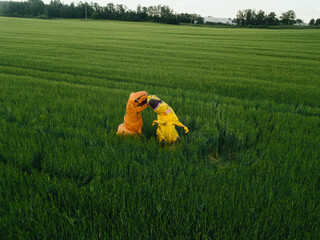 Two yellow and orange dinosaur dino tyrannosaurus running biting each other and having fun in green field. Shot from air. aerial shot. Dinosaur playing small guitar