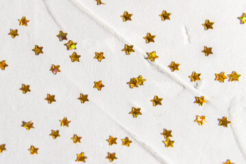 Shiny golden stars are scattered on a light concrete background. Place for text.