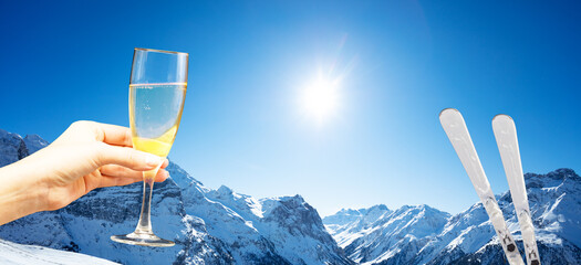 Ski and hand hold glass of champagne over the Alps mountain snow range on the good sunny weather