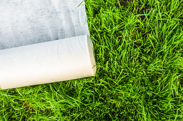 A roll of white geotextile lies on the green grass outside