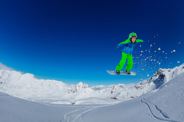 Little boy jump on snowboard over blue sky with snow powder fly, mountain range tops on background