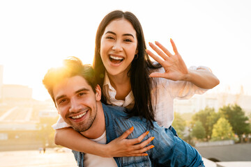 Wall Mural - Image of cheerful couple piggybacking ride and waving hand