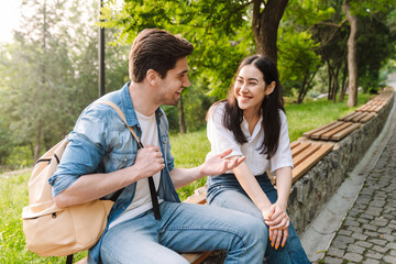 Wall Mural - Image of couple talking and smiling at each other while sitting on bench