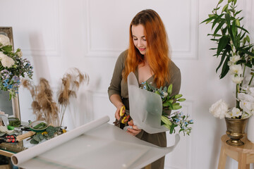 Wall Mural - Girl florist with red hair makes a beautiful bouquet in a flower shop of lilies and red flowers