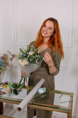 Wall Mural - Beautiful girl with red hair in a blue print dress with flowers smiles in the photo and hold a beautiful gift bouquet