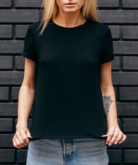 Wall Mural - Stylish blonde girl wearing black t-shirt and glasses posing on black wall background, urban clothing style. Street photography