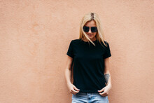 Stylish Blonde Girl Wearing Black T-shirt And Glasses Posing Against Street , Urban Clothing Style. Street Photography