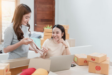 Two beautiful Asian women are checking orders by laptops via the internet. And pack the paper box With a happy smiling face, being a new normal online business