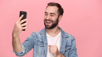 Wall Mural - Young man guy 20s in denim jacket white t-shirt using mobile cell phone doing selfie videoconference conducting pleasant conversation isolated on pastel pink background studio People lifestyle concept