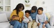 © VAKSMANV - Happy African American family sitting on sofa using tablet at home.