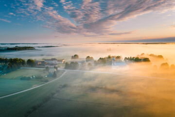 Majestic church covered in fog and surrounded by forest. Aerial view over picturesque countryside with at sunrise with long light rays. 